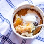 A ramekin of a mini-peach cobbler with ice cream on top.