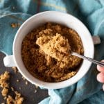 A small bowl of freshly made brown sugar with a spoon holding some of it up close.
