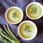3 bowls of cream of asparagus soup, garnished with chives and fresh dill. A few asparagus are off to the side.