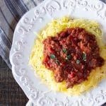 White platter heaped with golden spaghetti squash cooked in the air fryer, and topped with a meatless hearty tomato sauce.