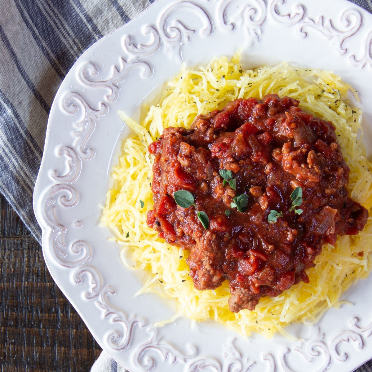 White platter heaped with golden spaghetti squash cooked in the air fryer, and topped with a meatless hearty tomato sauce.