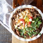 Tamale pie with cornbread on the bottom, and Beyond Beef sauce on top. The tamale pie is topped with melted cheese, cilantro, tomatoes, avocado, enchilada sauce and jalapeño slices.