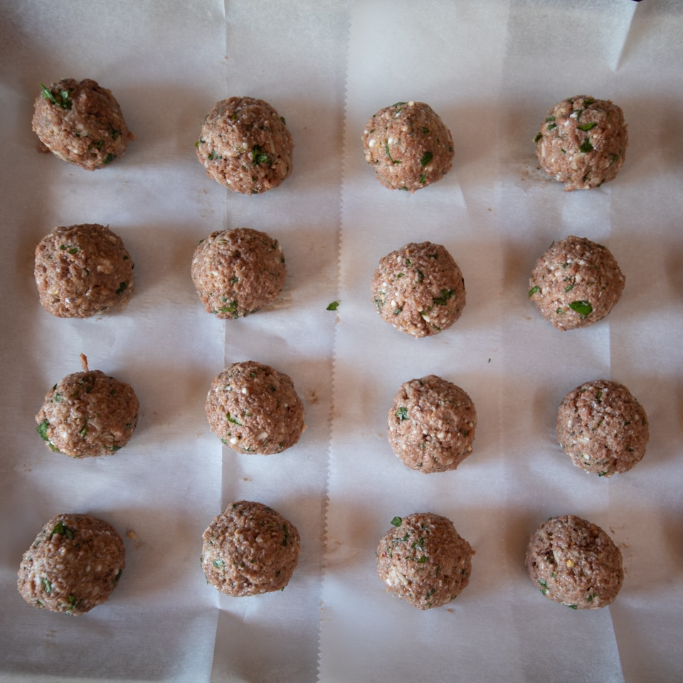 Meatball made with Beyond Beef arranged on a parchment lined baking sheet, ready to go in the oven.