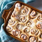 Cinnamon rolls smeared with icing, nestled in a baking dish.