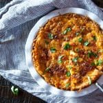 A baking dish of a vegetarian Quiche Lorraine with a hash brown crust, with one piece being lifted out.