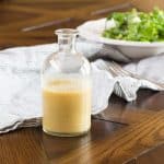 A small bottle of homemade pear vinaigrette, with a green salad in the background.