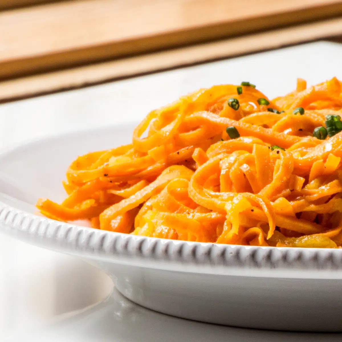 A dish of spiralized sweet potatoes and apples cooked in butter, topped with chives.