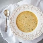 A fancy white bowl filled with creamy vegetarian broccoli cheddar soup, with a soup spoon.