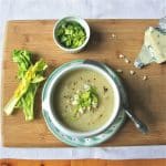 A bowl of celery root soup, topped with celery tops, gorgonzola cheese and ground black pepper.
