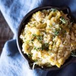 A small cast iron pot holding leek confit with thyme leaves sprinkled on top.