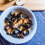 A bowl of cooked mussels in a coconut curry sauce.