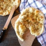 Two pizza bread rounds seasoned aglio (garlic) and olio (olive oil) style. One round has a piece torn from it.