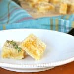 Lemon bars with coconut and shortbread, with a twig of thyme, arranged on a plate.