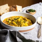A bowl of vegetarian barley soup with potatoes and mint, with some bread and a spoon.
