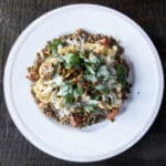 Lentil salad on a plate, topped with cauliflower steak, pumpkin seeds, parsley and a lemon tahini dressing.