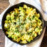 A skillet of pasta cooked with romanesco and apples, topped with Parmesan cheese and breadcrumbs.