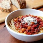 A bowl of spaghetti topped with a tomato sauce, chickpeas and Parmesan cheese.