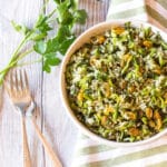 A bowl of cooked rice tossed with fresh herbs, scallions and raisins.