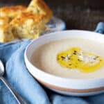 A bowl of cheesy cauliflower soup with rosemary oil drizzled on top.