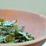 A wooden bowl of crispy seasoned kale chips.