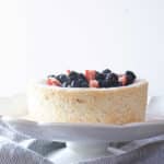 Angel food cake on a cake stand, topped with berries.