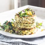 Three corn and zucchini fritters stacked on top of each other, and topped with a kale, avocado and mango salad.