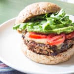 Spicy bean burger make with black beans topped with cheese, tomatoes and lettuce on a plate.