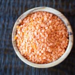 A wooden bowl filled with dried red lentils.