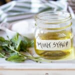 A jar of mint simple syrup with mint leaves and sugar.