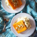 Butternut squash steaks on plates with mashed potatoes. the steaks are topped with roasted garlic and sage.