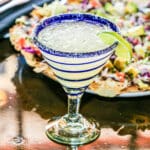 A glass with a salted rim and a slice of lime filled with a margarita on the rocks.