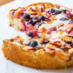 Summer peach cake topped with fresh peaches and blueberries on a marble counter.