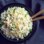 A bowl of cauliflower rice sauteed with carrots with 2 serving spoons.