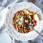 A white bowl filled with Mediterranean chickpea salad with toasted na'an bread.