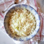 A blue and white bowl filled with buttermilk coleslaw with a serving spoon.