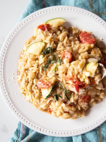 One-pot pasta dish of tomatoes, zucchini, corn, pesto, and mozzarella mixed into orzo on a white plate.